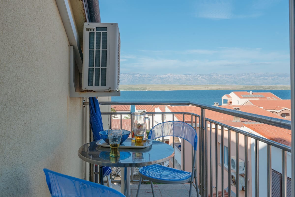 Ein Balkon mit Tisch und Stühlen, mit Blick auf ein Gewässer und Gebäude.