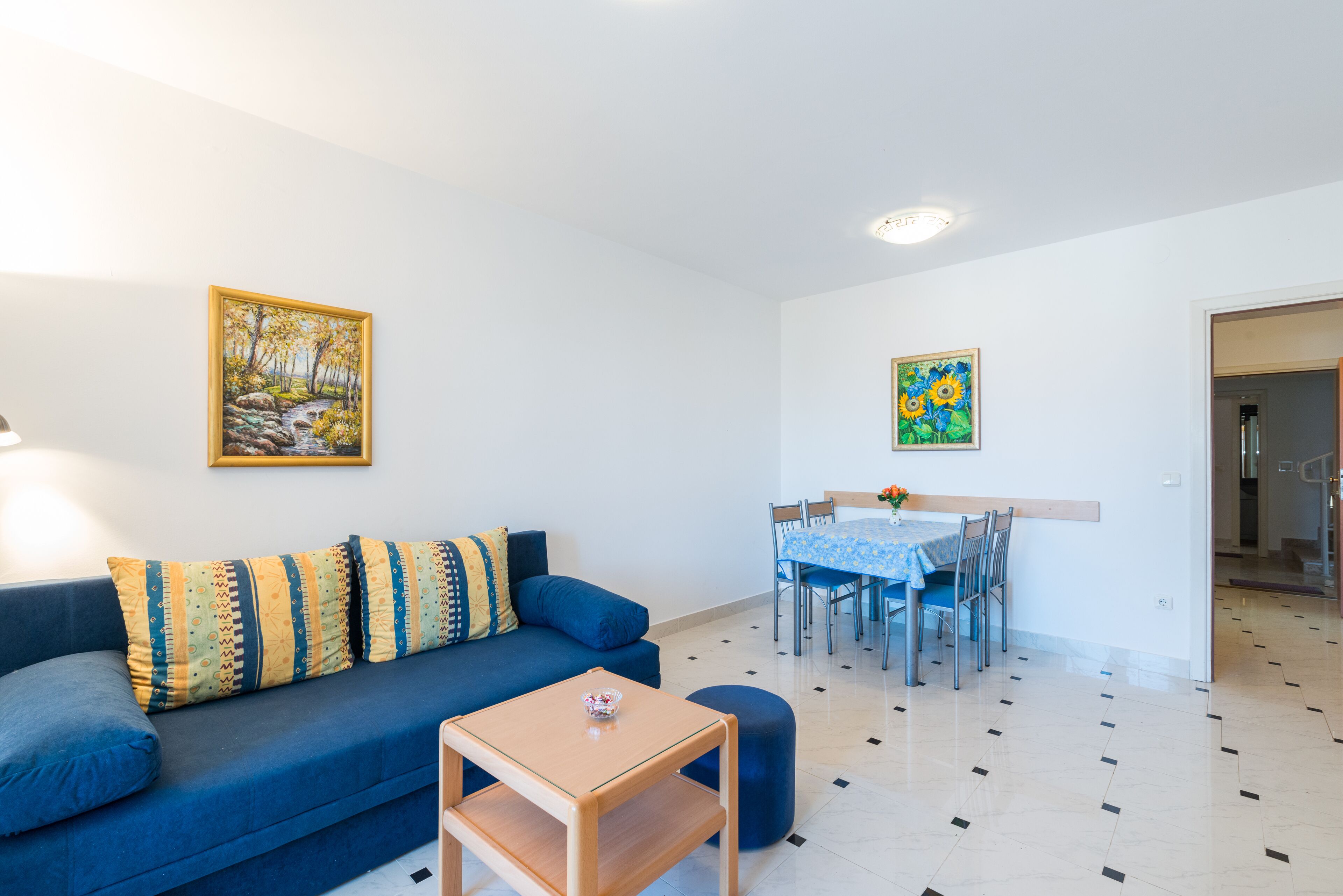 Un salon avec un canapé bleu, une petite table en bois et un coin repas comprenant une table et des chaises.