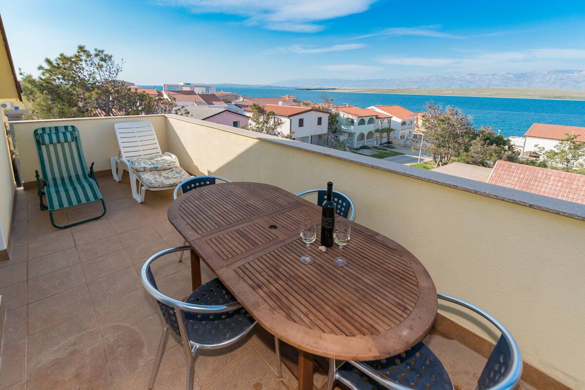 Ein Balkon mit einem Holztisch, zwei Stühlen und einer gestreiften Liege.