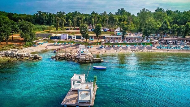 Une propriété située au bord de l’eau, dotée d’un quai, d’une eau cristalline et d’installations de plage, notamment des chaises longues et des parasols.