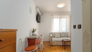 A compact living space with a kitchenette, a dining area with chairs, a sofa, and a small table. - Funtana Apartments Budinjaš  (FUNTANA)