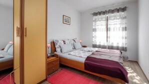Ein Schlafzimmer mit Bett, Nachttischen, einem Kleiderschrank, einem roten Teppich und einem Fenster mit Vorhängen.