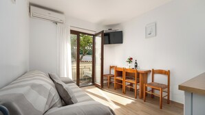 Ein Zimmer mit einem Bett, einem Schreibtisch mit zwei Stühlen, einem an der Wand befestigten Fernseher und einer Glasschiebetür, die zu einem Außenbereich führt.