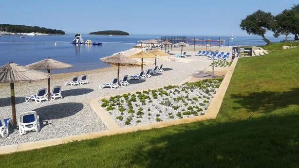 A beachside resort with sun loungers, umbrellas, and a clear view of the sea. -  Funtana Apartments Budinjaš  (FUNTANA)