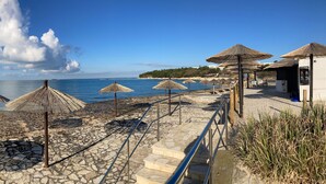 A beachside area with stone flooring, thatched umbrellas, and a clear view of the sea. -  Funtana Apartments Budinjaš  (FUNTANA)
