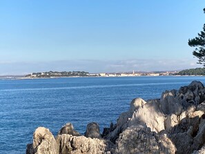 Blick auf die Küste mit Felsformationen im Vordergrund und einer entfernten Stadtlandschaft über dem Wasser.