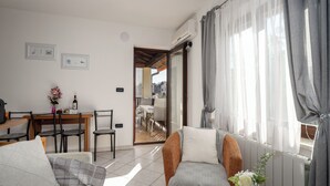 A modern living room with a sofa, armchairs, and a dining table. There is a sliding glass door leading to an outdoor area. -  Funtana Apartments Budinjaš  (FUNTANA)
