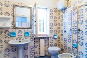 A bathroom with floral patterned tiles, a white sink, a toilet, and a shower area. - Appartamento Arancio (Marciana)