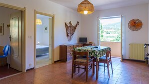 A dining area with a table, chairs, a hanging light fixture, and a view through a window. - Appartamento Arancio (Marciana)