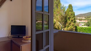 A room with a television on a wooden cabinet, a basket of fruit, and a view of trees and buildings through a window. - Appartamento Arancio (Marciana)