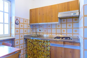 A kitchen with wooden cabinets, a gas stove, and a sink. - Appartamento Arancio (Marciana)
