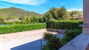 A courtyard with a view of a mountain, surrounded by greenery and a paved area. - Appartamento Arancio (Marciana)