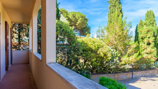 A covered outdoor corridor with a tiled floor, bordered by a low wall and a row of windows. - Appartamento Arancio (Marciana)
