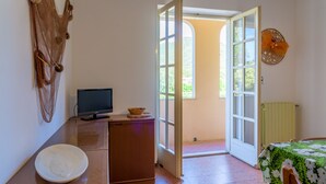 A room with a desk, a bowl, a television, and a door leading outside. - Appartamento Arancio (Marciana)
