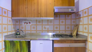 Een kleine keuken met houten kastjes, een ingebouwde gasoven, een witte koelkast en een spoelbak.