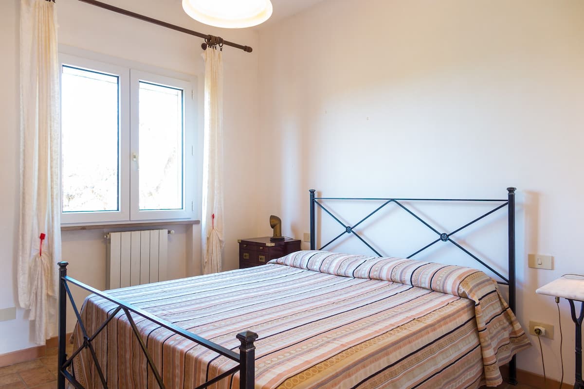 Een slaapkamer met een bed, gordijnen, een raam en een radiator.