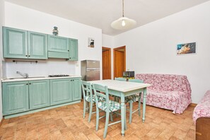 Une cuisine compacte avec des meubles de couleur turquoise, une table à manger avec des chaises, un four à micro-ondes et un réfrigérateur.