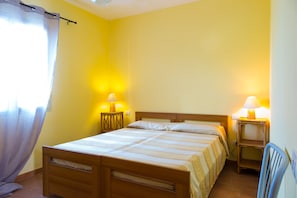 Habitación individual con una cama de madera, dos mesitas de noche con lámparas y una cortina en la ventana.