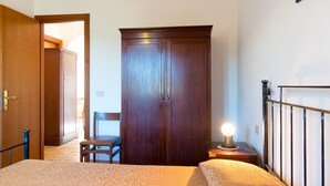 A bedroom with a bed, a wooden wardrobe, a chair, and a bedside table with a lamp. - Appartamenti Il Mare e La Quiete (Portoferraio)