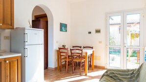 A kitchen with a refrigerator, wooden cabinets, a dining table with chairs, and a view through a glass door. - Appartamenti Il Mare e La Quiete (Portoferraio)