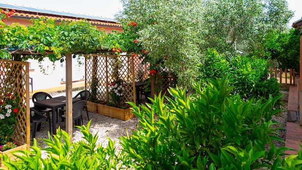 An outdoor patio with a wooden pergola, a table with chairs, and various plants. - Appartamenti Il Mare e La Quiete (Portoferraio)