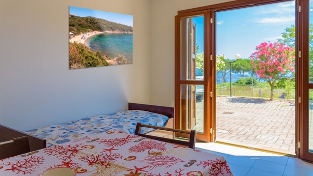 Un dormitorio con cama, ventana con vista a la playa y puerta que da a un espacio al aire libre.