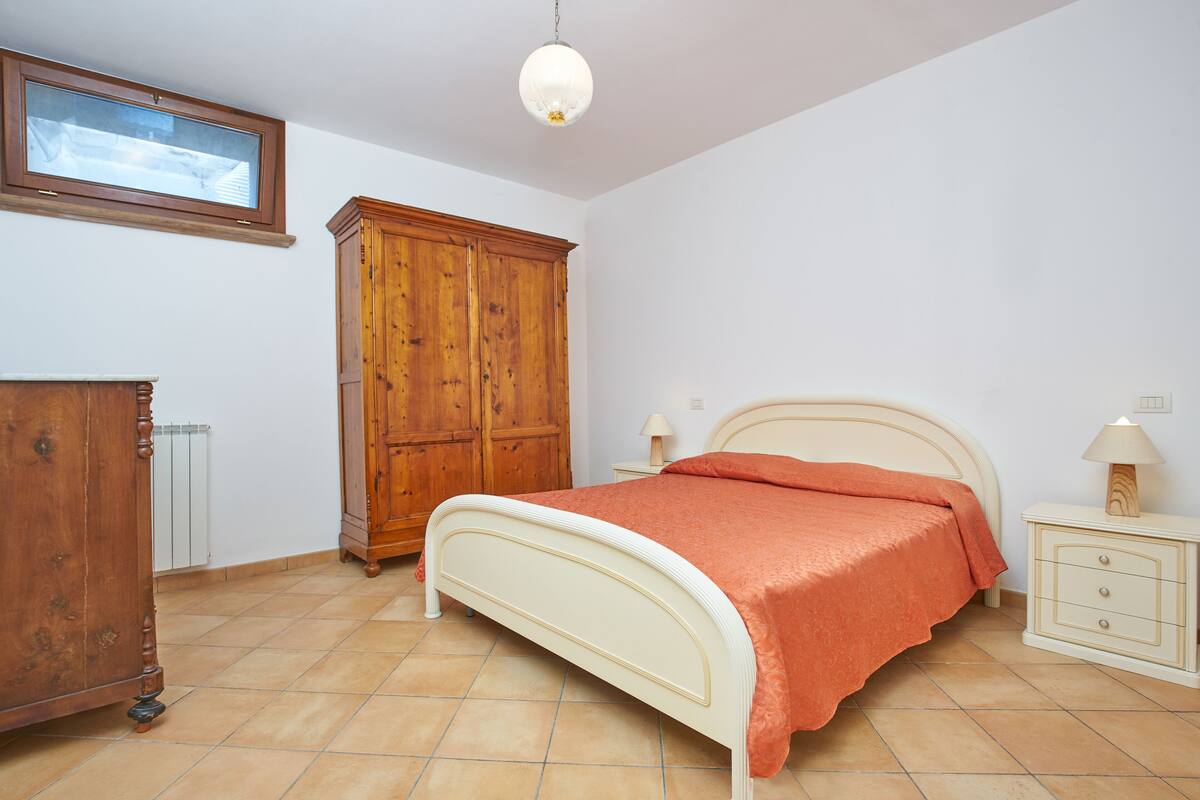 A bedroom with a bed, wooden wardrobe, nightstand, and a window with blinds.