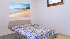 Un dormitorio con cama, televisor montado en la pared y un cuadro con una escena de playa.