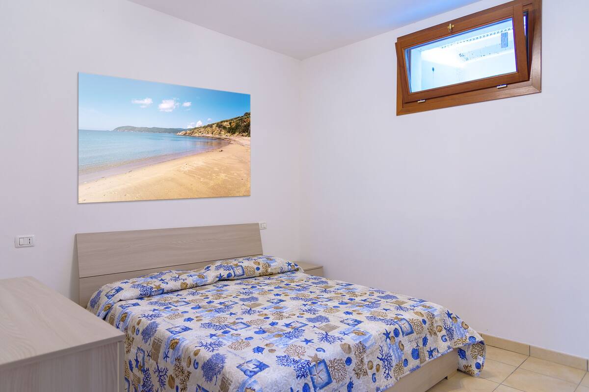 A bedroom with a bed, a TV mounted on the wall, and a beach scene painting.