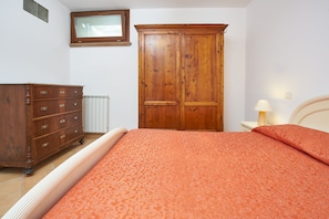 A bedroom with a bed, wooden wardrobe, dresser, and a nightstand with a lamp.