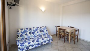 Ein Zimmer mit einer Couch, einem Esstisch mit Stühlen, einem Wand-Fernseher und einer Wandleuchte.