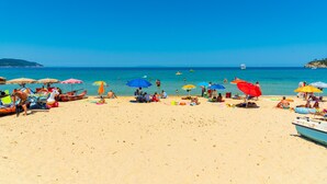 Een strand met mensen, parasols en boten.