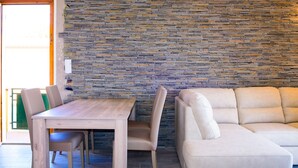A room with a stone wall, a wooden table, and a beige sofa. - Appartamento Elisa (Portoferraio)