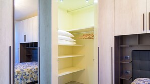 A bedroom with a bed, a closet with shelves, and a bedside table. - Appartamento Elisa (Portoferraio)