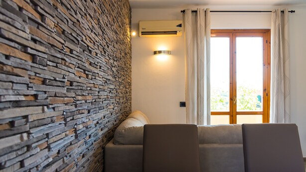 A room with a stone wall, a sofa, a table, and a window with curtains. - Appartamento Elisa (Portoferraio)