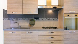 A modern kitchen with wooden cabinets, a stainless steel sink, a gas stove, and a built-in oven. - Appartamento Elisa (Portoferraio)
