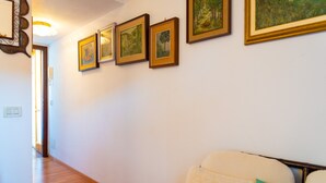 A hallway with wooden flooring, a bed with a headboard, and four framed paintings on the wall. - Appartamento La Via Del Mare (Rio)