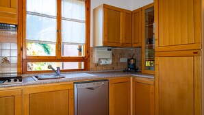 A kitchen with wooden cabinets, a dishwasher, a window with a curtain, and a countertop with a coffee maker. - Appartamento La Via Del Mare (Rio)