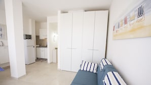 Una sala de estar moderna con un sofá, una cocina al fondo y un amplio armario blanco.