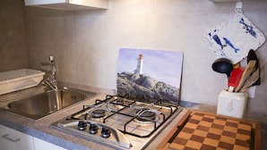 Una cocina con estufa a gas, pileta de acero inoxidable y tabla de cortar a cuadros.