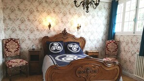 A classic bedroom with a wooden bed, floral wallpaper, and a chandelier. - Chambres d'Hôtes Au Cœur De Breizh (Plouguernevel)