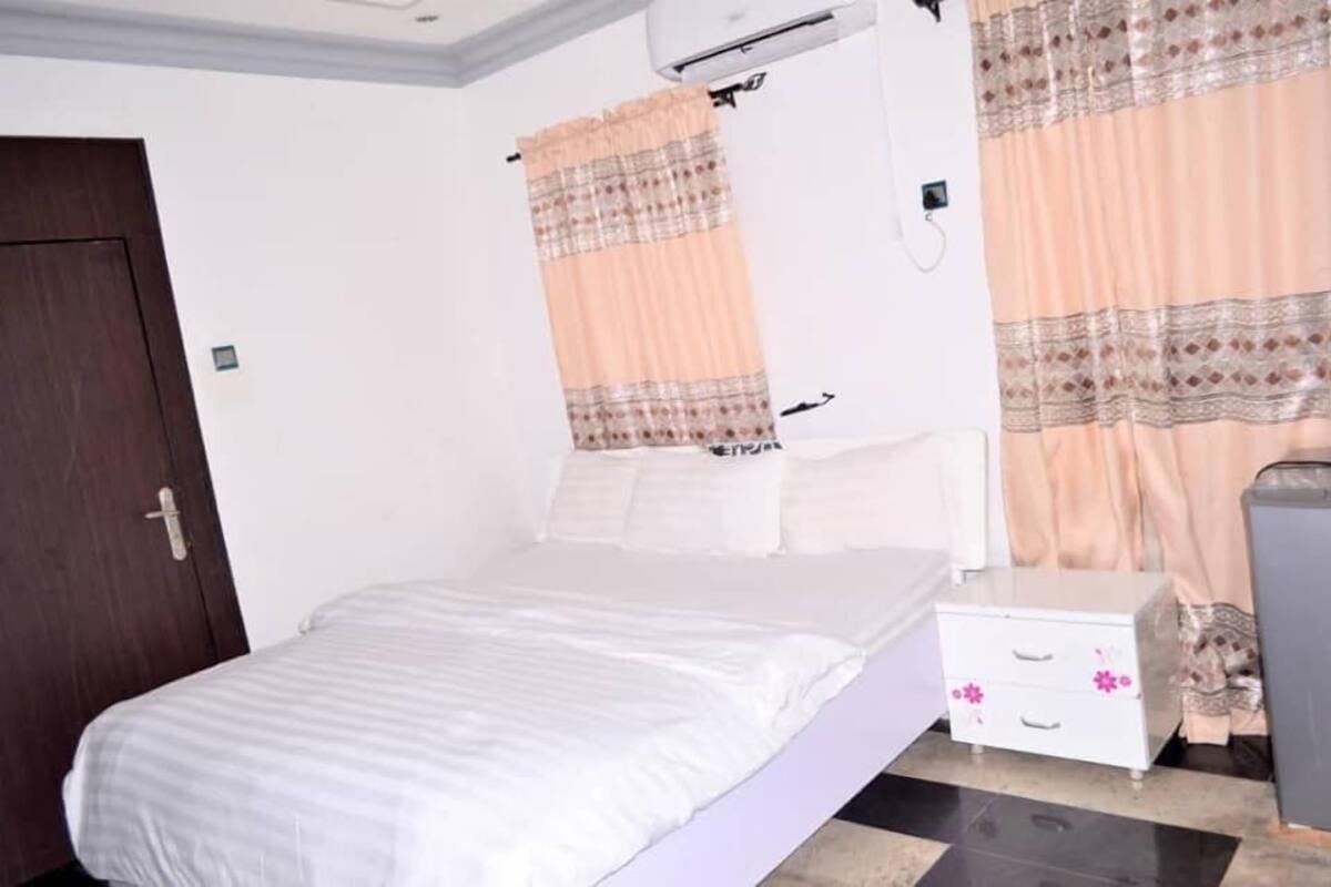 A bedroom with a bed, a nightstand, a wardrobe, and a window with curtains.
