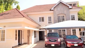 A two-story house with a red-tiled roof, a covered driveway, and two parked cars. - Big Pepper Apartment (Abuja)
