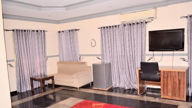 A hotel room with a bed, a sofa, a desk, a TV, and curtains. - Big Pepper Apartment (Abuja)