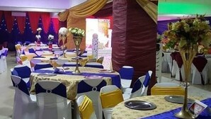 A banquet hall with tables set for events, draped with golden fabric, and decorated with floral centerpieces. - Big Pepper Apartment (Abuja)