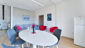Una sala de estar moderna con una mesa redonda blanca, sillas azules y rojas, un sofá gris y un refrigerador blanco.