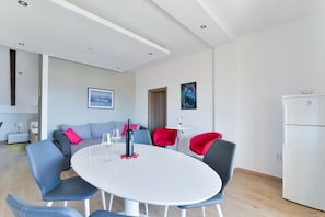 A modern living room with a round white table, blue and red chairs, a grey sofa, and a white refrigerator. - Apartments Medved (Vir)