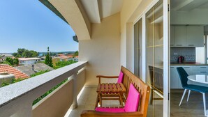 Un balcón con banca de madera y una mesa, una zona de cocina con armarios, y vistas al barrio.