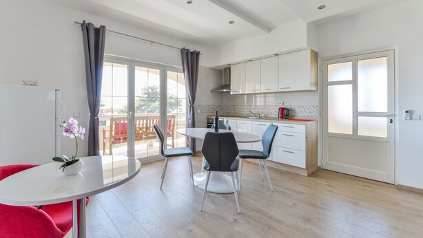 Una cocina moderna con armarios blancos, una mesa de comedor redonda y una silla roja.