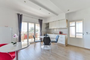 A modern kitchen with white cabinets, a round dining table, and a red chair. - Apartments Medved (Vir)